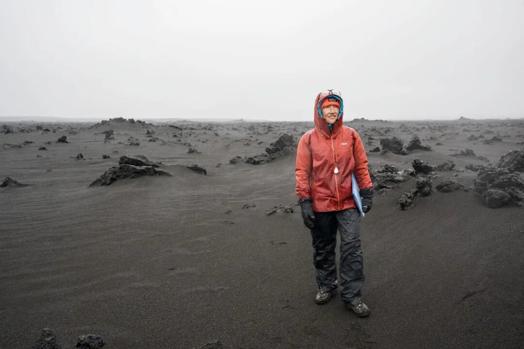 阿尔忒弥斯二号任务专家克里斯蒂娜·科赫（Christina Koch）在冰岛进行地质训练时，站在一片风势强劲的火山地貌中；该火山地形被用作月球地貌的类比环境。